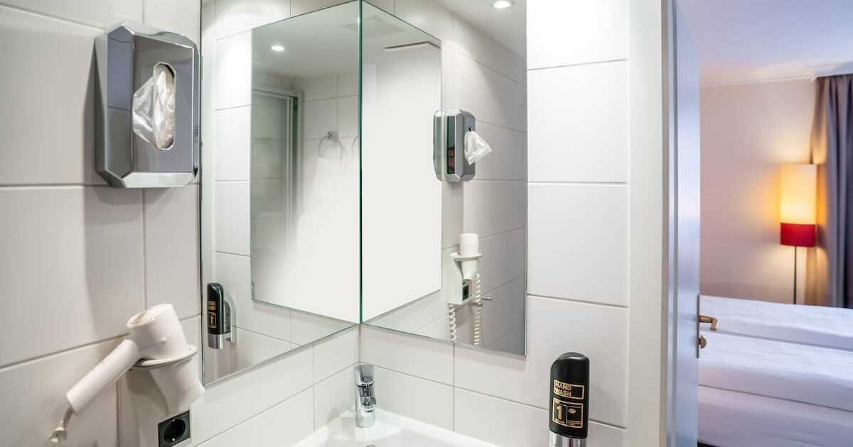 Hotel_Europaeischer_Hof_Doppel_Standard_City_Badezimmer_2 Ausschnitt aus einem Badezimmer mit Föhn, Spiegel und Waschbecken in einem günstigen Doppelzimmer in München
