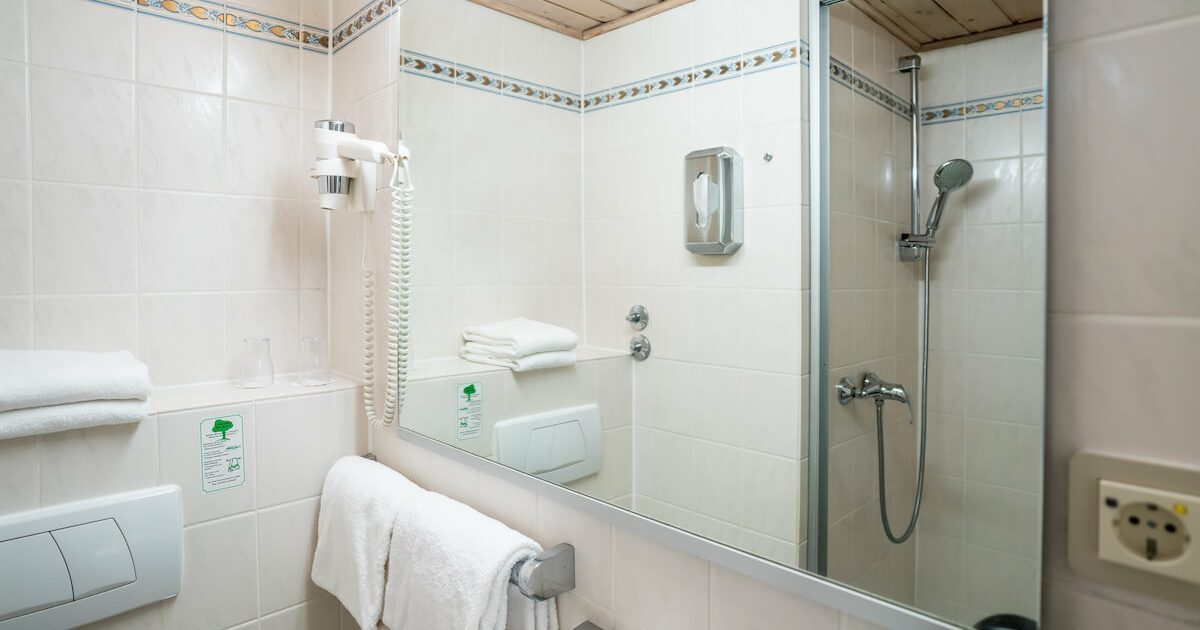 Hotel_Europaeischer_Hof_Einzel_Grand_Lit_fuer_2_Gaeste_Badezimmer_2 Ausschnitt eines Badezimmers mit Föhn und einem Spiegel in welchem sich die Dusche spiegelt in einem günstigen Doppelzimmer in München