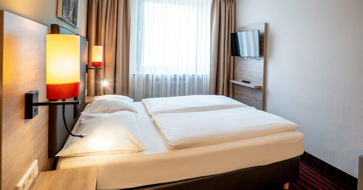 Helles und günstiges Doppelzimmer in München mit Bett, beigen Vorhängen und einem Fernseher