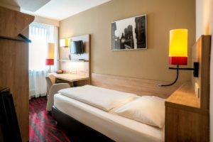 Blick in das helle, moderne & ruhige Hotelzimmer Helles und voll ausgestattetes Einzelzimmer mit Bett, Schreibtisch, Stuhl und Fernseher in einem günstigen und zentralen Hotel am Hauptbahnhof in München