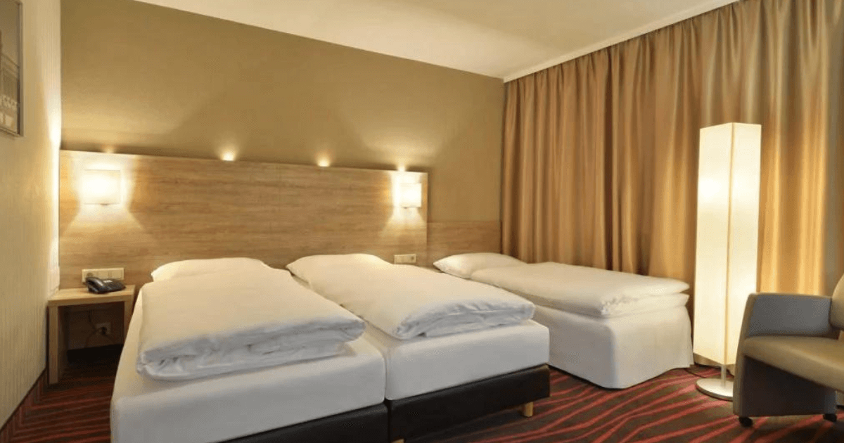 HEH_Dreibettzimmer_2 Modernes und günstiges Dreibettzimmer in München mit zugezogenen beigen Vorhängen und leuchtenden Lampen