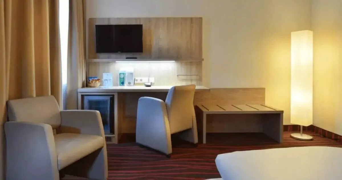 Ausschnitt aus einem günstigen Dreibettzimmer in München mit Schreibtisch, Stuhl, Sessel, Kühlschrank und Kofferablage
