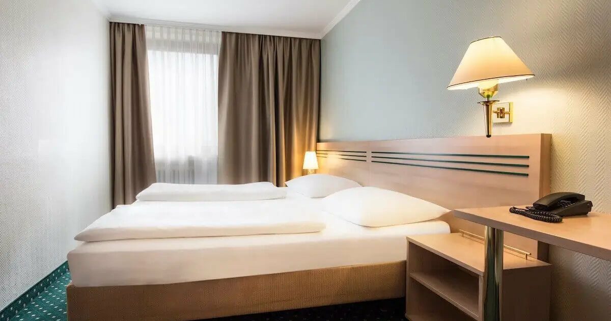 HEH-Doppel-Urban-Smart Helles und günstiges Doppelzimmer in München mit Bett, beigen Vorhängen und Kommoden aus hellem Holz. Günstig übernachten in München