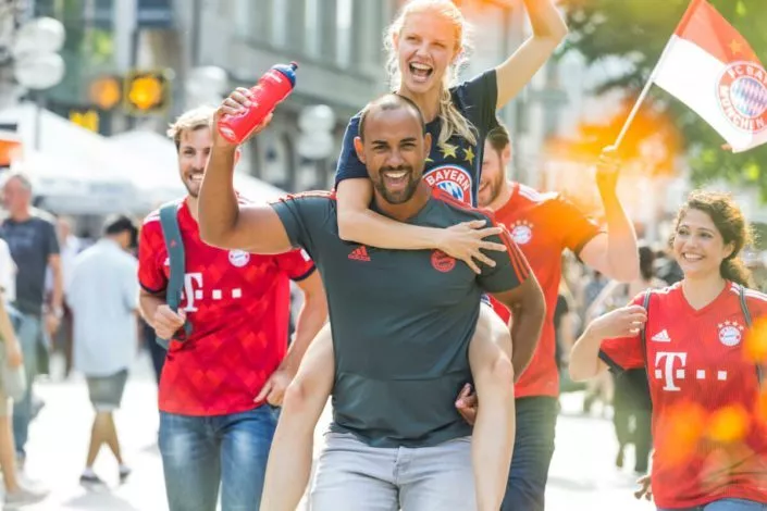 Eine Gruppe Fußballfans in den Trikots des FC Bayern Münchens mit einer Flagge und einer Trinkflasche