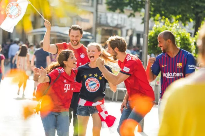 Eine Gruppe Fußballfans mit Bayern und Barcelona Trikots und einer FC Bayern Flagge