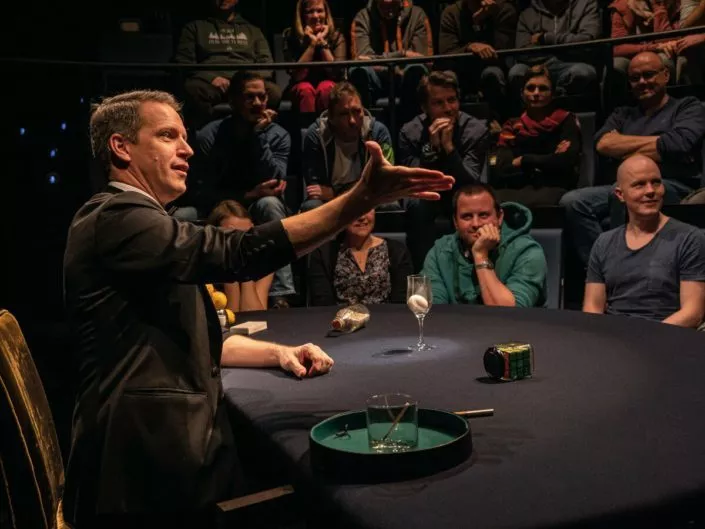 Table Magic Theater Alexander Krist bei einem Zaubertrick mit dem Publikum im Hintergrund