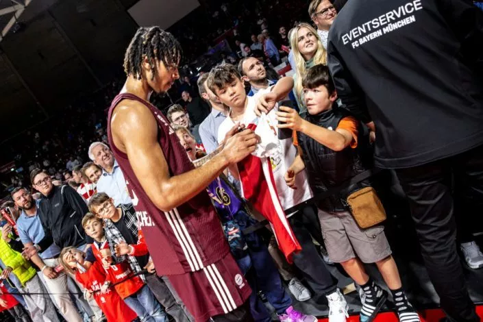 Basketball München - ein Spieler gibt jungen Fans Autogramme