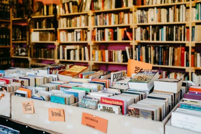 Viele Bücher in Holzboxen im Vordergrund und ein Bücherregal im Hintergrund