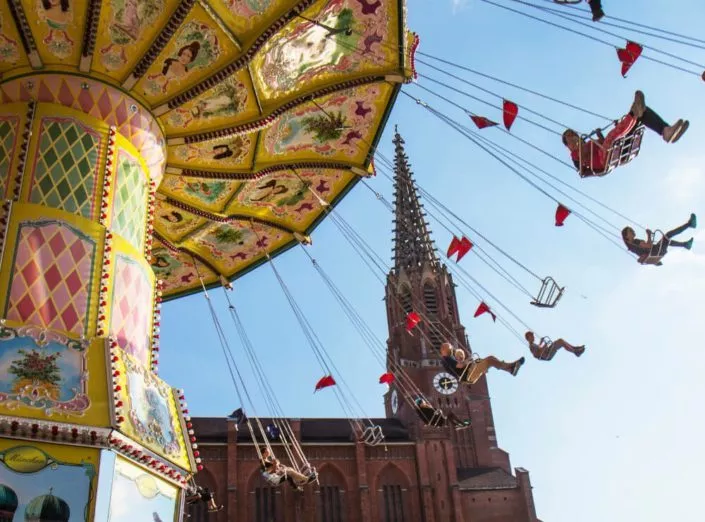 Fahrendes Kettenkarussell vor einer roten Kirche auf dem Mariahilfplatz in München