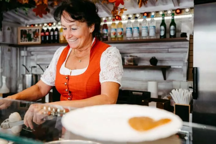 Verkäuferin in Tracht an einem Essensstand, welche gerade das Essen zubereitet,