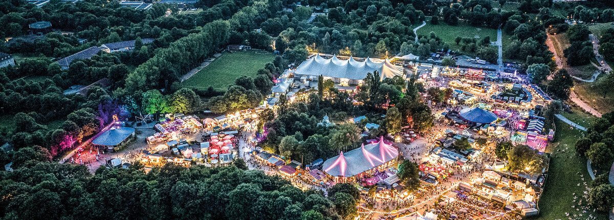 twso2022-festivalansicht-drohne-c-antonbrandl-300rgb Drohnenaufnahme des Tollwood Sommerfestivals in München mit Festivalbühnen, bunten Zelten und zahlreichen Besuchern