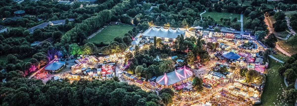 Drohnenaufnahme des Tollwood Sommerfestivals in München mit Festivalbühnen, bunten Zelten und zahlreichen Besuchern